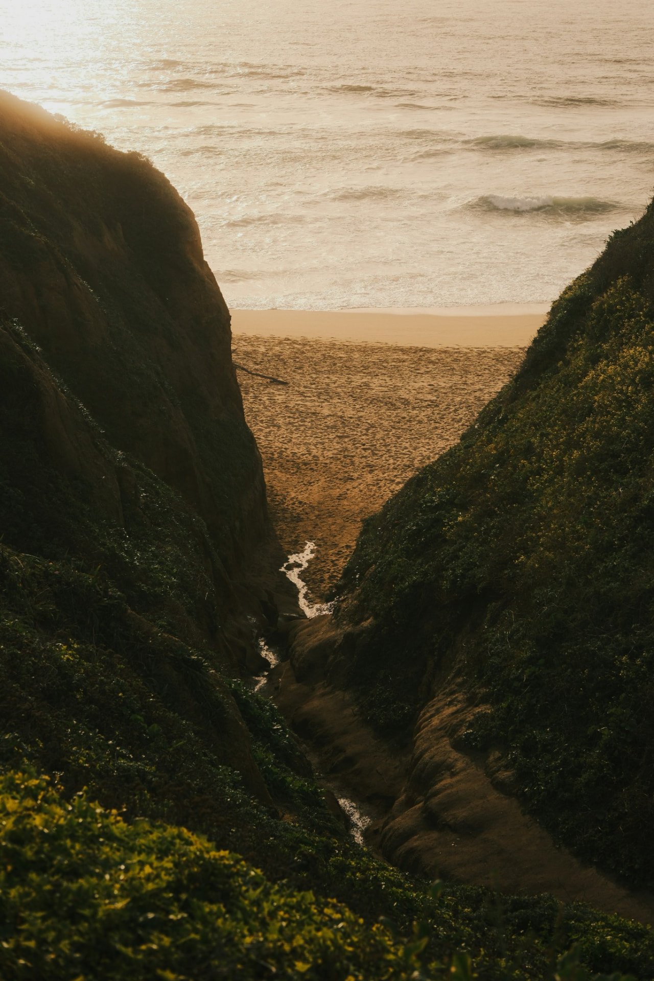 Blick durch eine Felsenschlucht auf einen Sandstrand und das Meer im Abendlicht